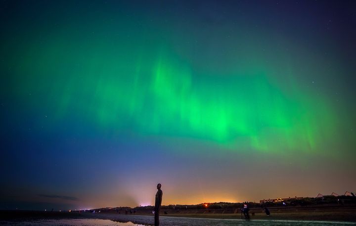 The northern lights glow on the horizon at Another Place by Anthony Gormley, Crosby Beach, Liverpool, Merseyside.