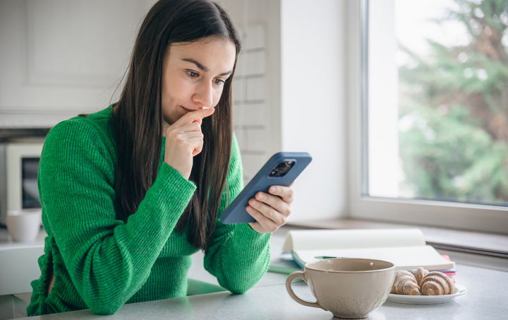 Woman in the kitchen in the morning with a smartphone and a cup of coffee