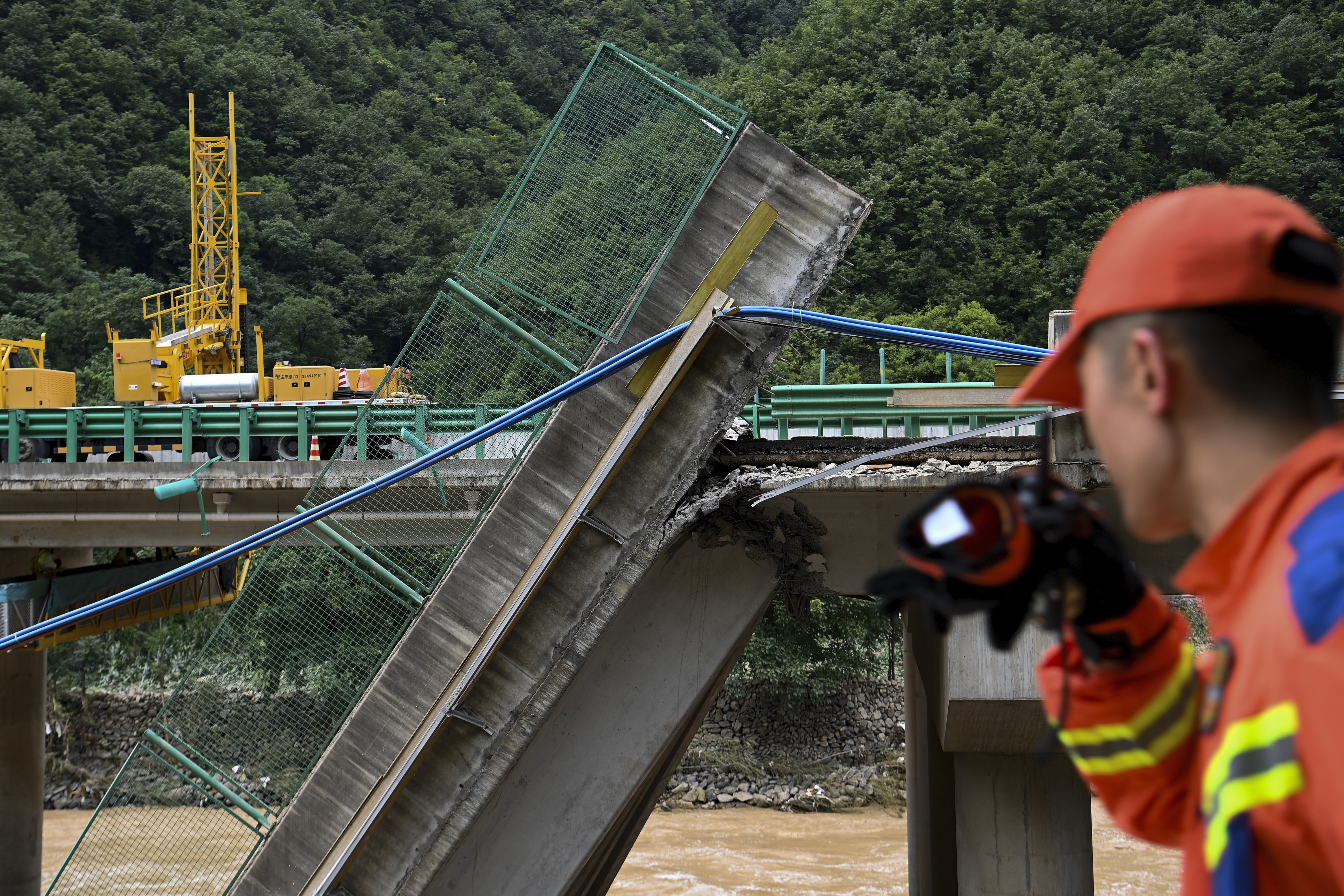 In this photo released by Xinhua News Agency, a rescuer looks at the collapsed bridge as they conduct a search and rescue on a river in Zhashui County in Shangluo City, northwest China's Shaanxi Province, Saturday, July 20, 2024.