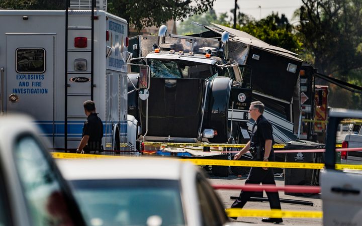 Police officers walk past the remains of an armored Los Angeles Police Department tractor-trailer July 1, 2021, after illegal fireworks seized at a home exploded in South Los Angeles.